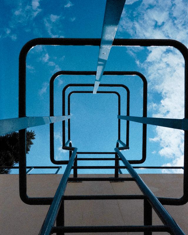 Looking up through a basketball hoop frame at a blue sky and a tall housing block.