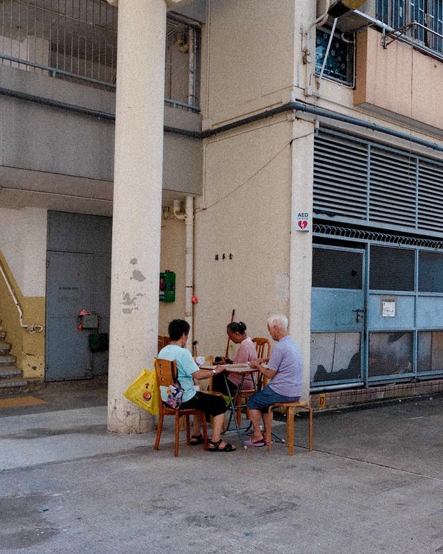 Three people sitting outside a shop in the shade of a Hong Kong building.