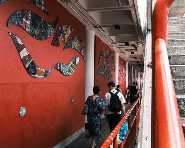 A red wall with a circular painted mural and figures passing in the foreground.