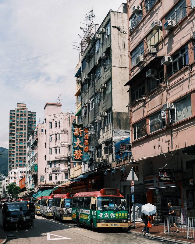 A green minibus and pedestrians on a narrow Hong Kong street lined with old buildings.