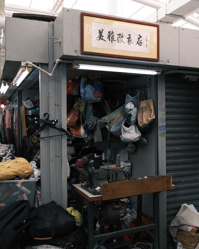 A shopkeeper standing among clothes and objects in a small Hong Kong shop.