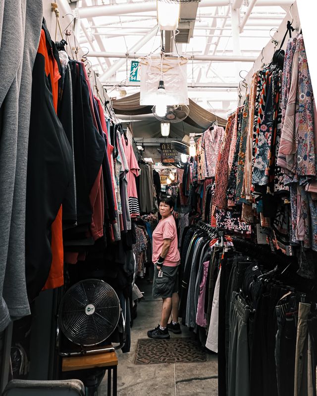 A narrow aisle of hanging clothes and bags inside a Hong Kong market.