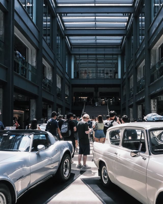 The polished side of a white car reflecting the crowd at an indoor car meet.