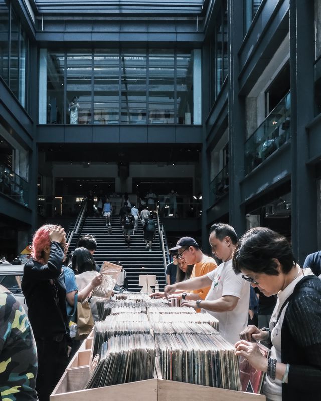 People browsing tables under the concrete canopy of an industrial building.
