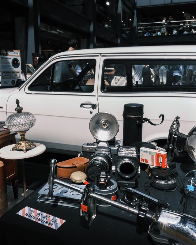 Vintage cameras and silver curios arranged on a market table beside a white van.