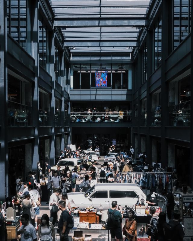 People inspecting cars and stalls at a busy indoor car meet.