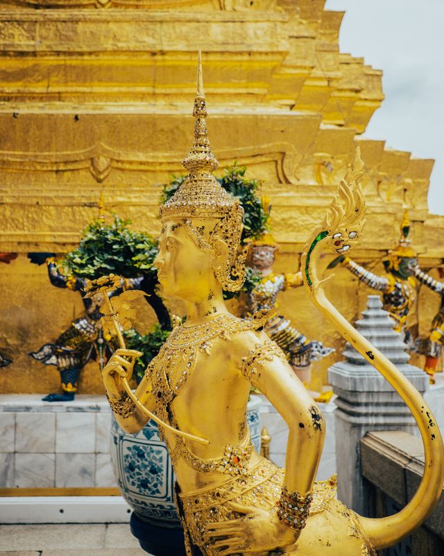 A gilded temple guardian statue surrounded by green foliage.