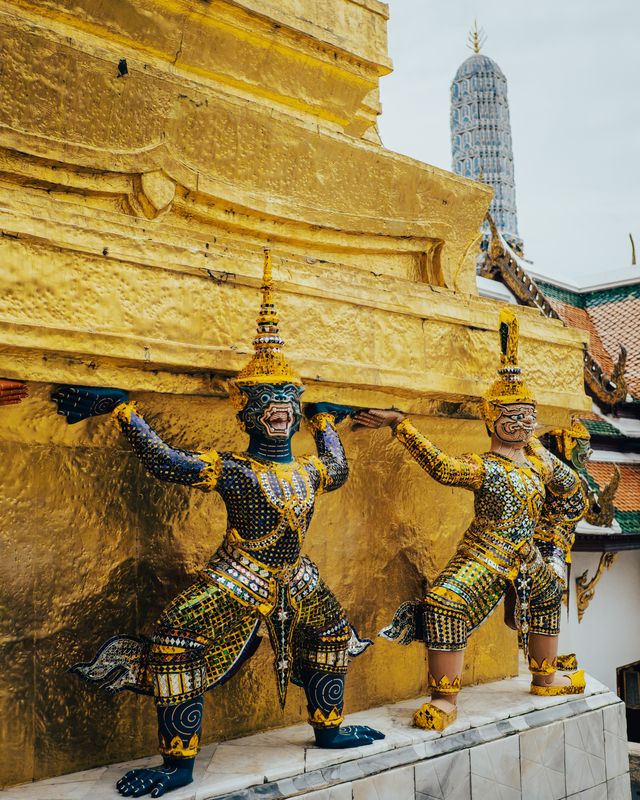 An ornate demon guardian statue in gold and green at a Bangkok temple.