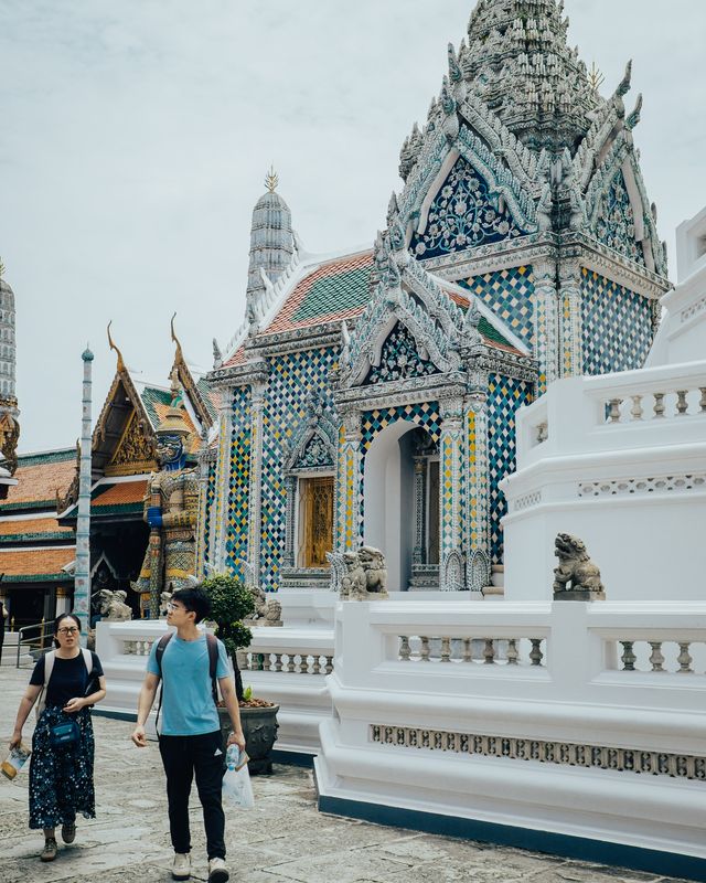 Two visitors walking past an ornate temple building with a patterned roof.