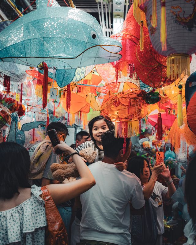 A crowd walking beneath a canopy of red and blue lanterns.