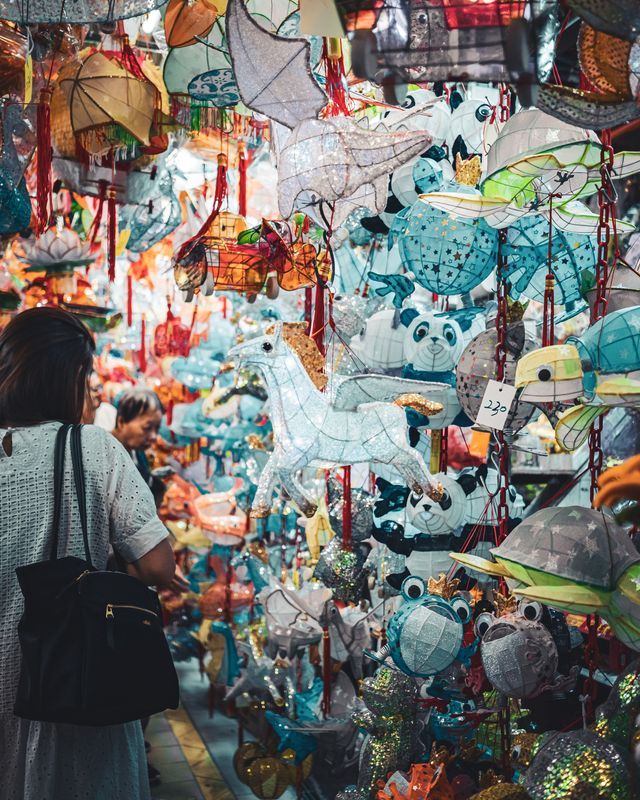A crowded festival street seen beneath hanging lanterns.