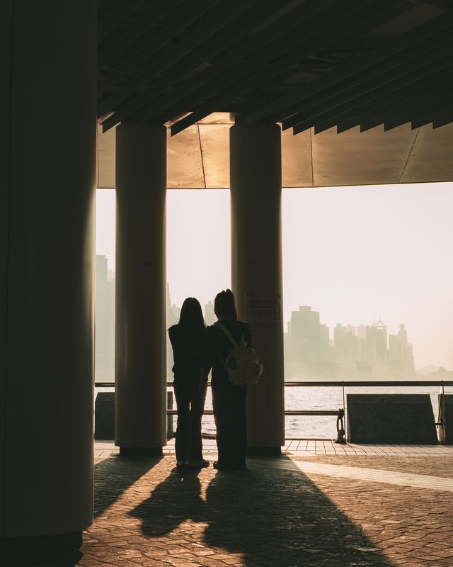 Two figures standing between tall pillars, framed by hard light and long shadows.