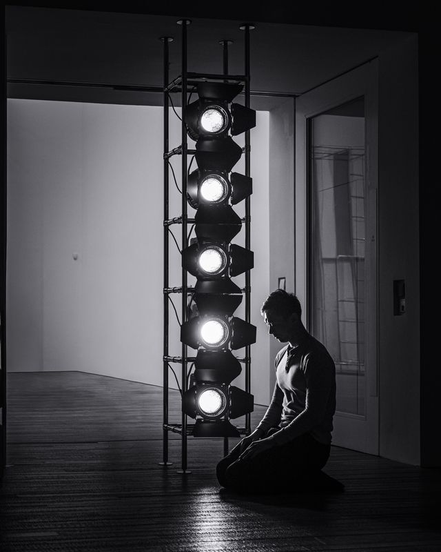 A dancer in a dark studio, lit by a single window.