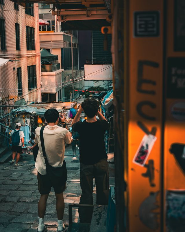 Two photographers working on a crowded Hong Kong street at dusk.