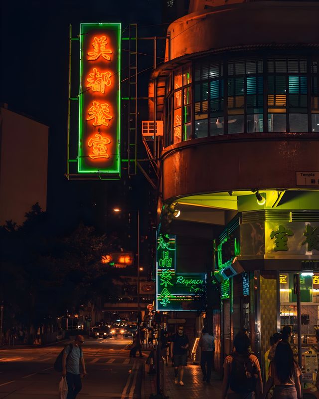 A Hong Kong street corner at night, with green and orange neon signs.
