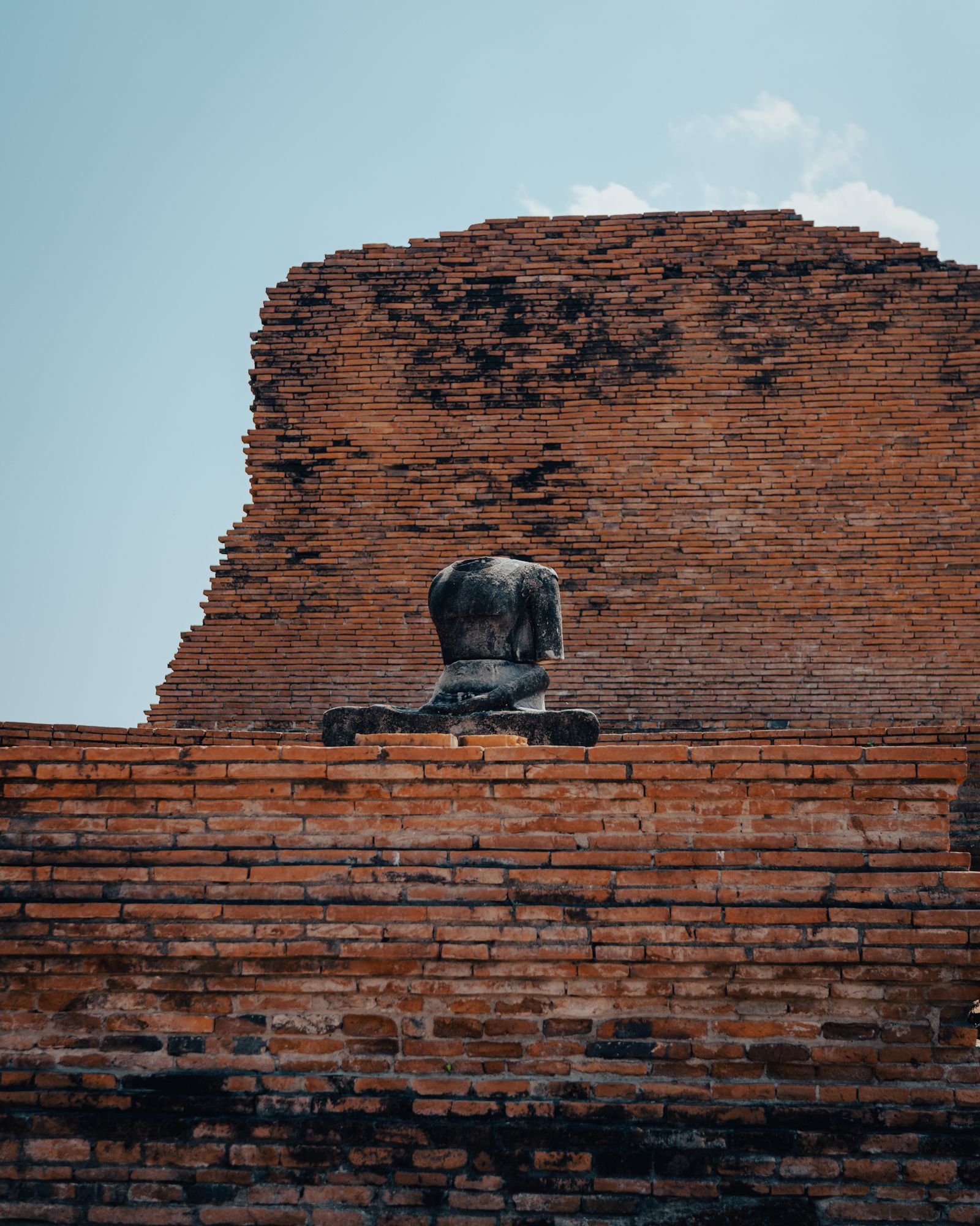 A Buddha statue seated in warm sunlight among ruins.