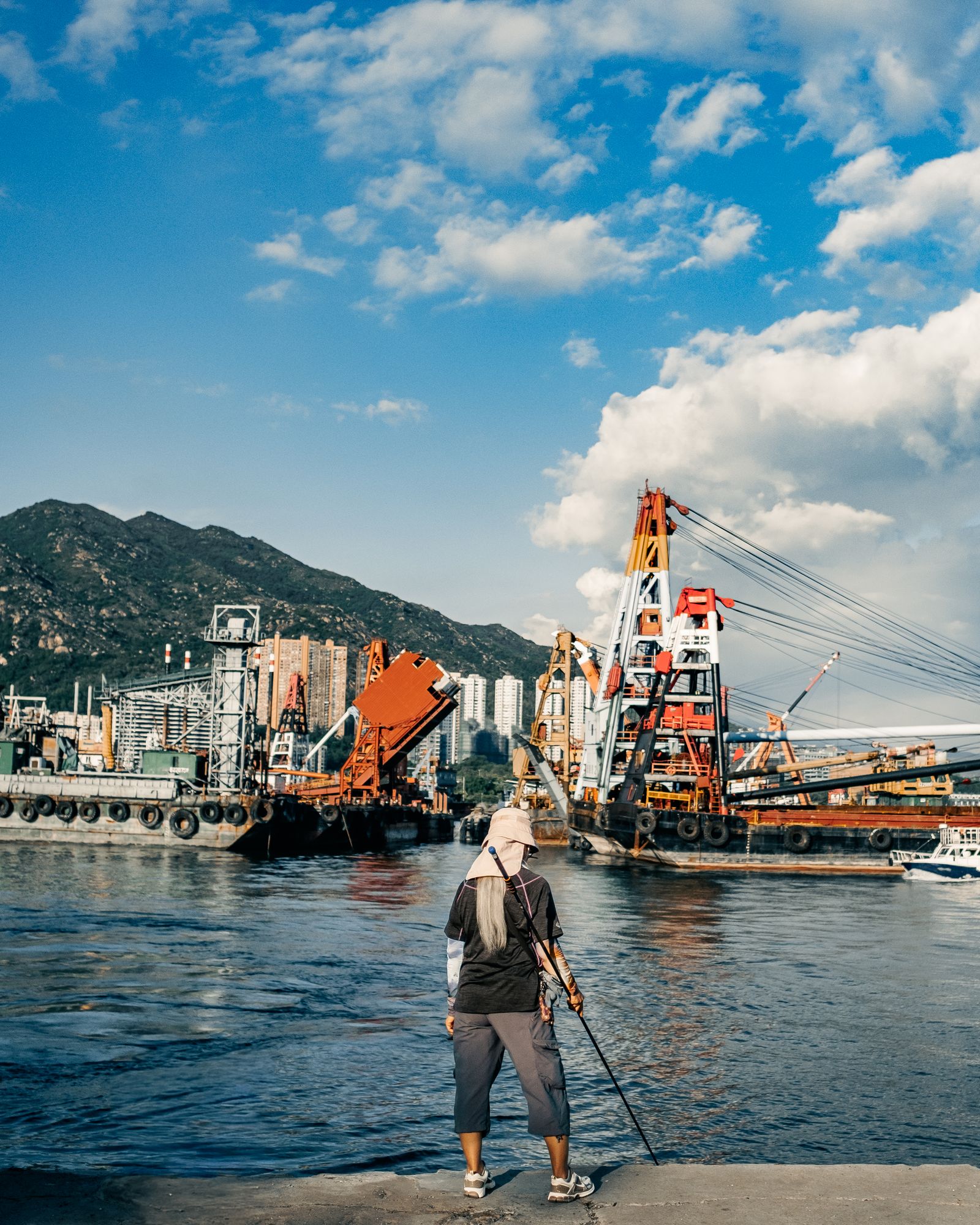 A man standing on a Hong Kong pier with boats and the harbour behind him.