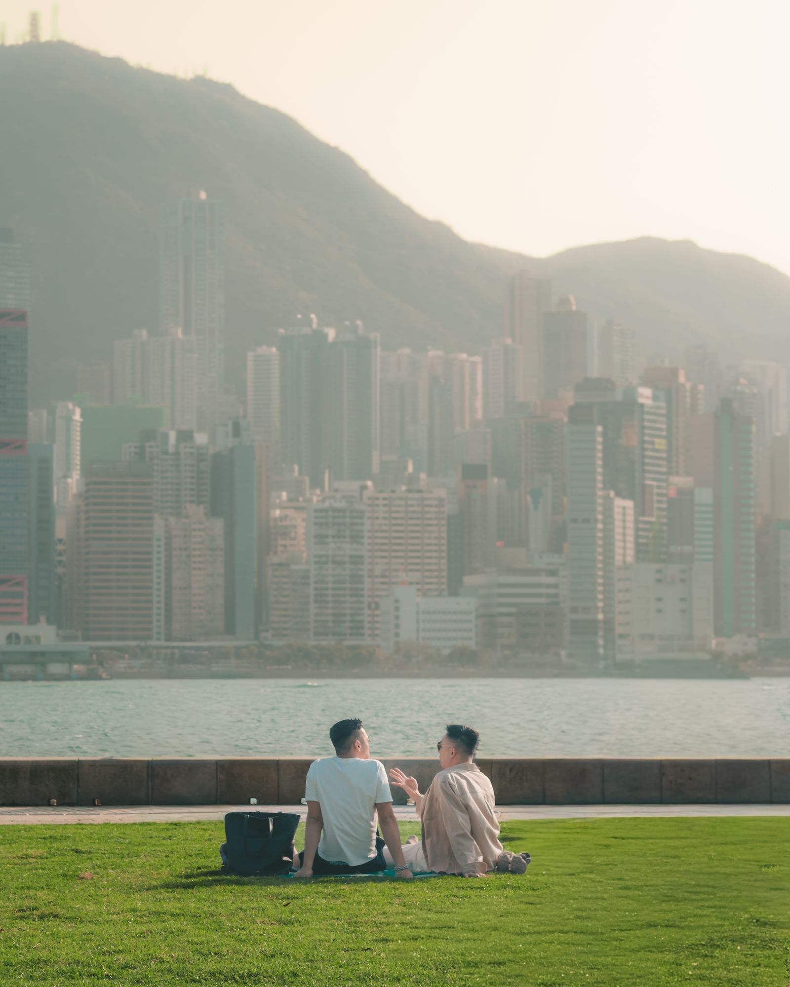 A couple sitting on a lawn beside the Hong Kong harbour.