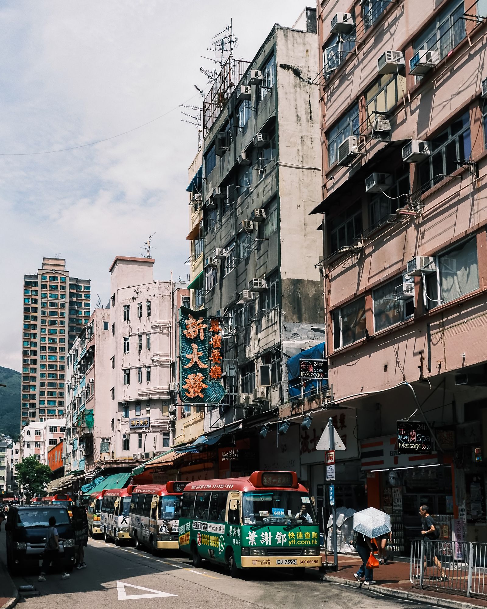 A green minibus and pedestrians on a narrow Hong Kong street lined with old buildings.