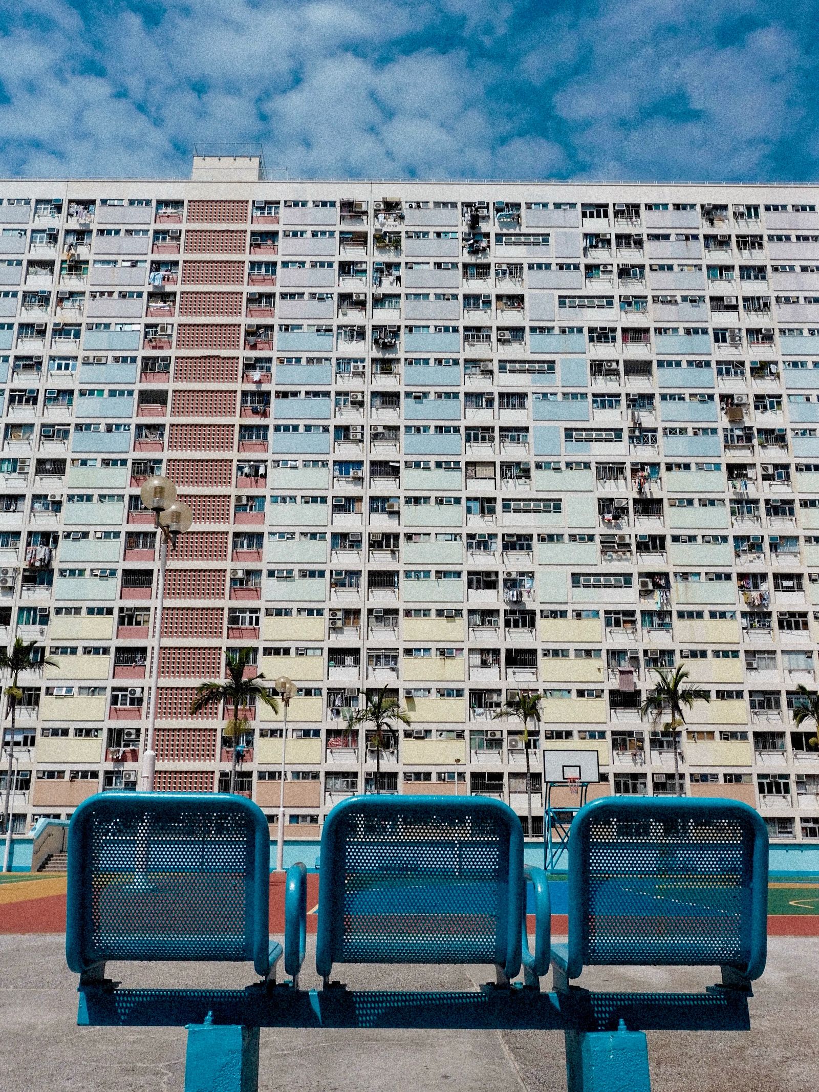 Blue benches in the foreground of a dense public housing estate under a bright sky.