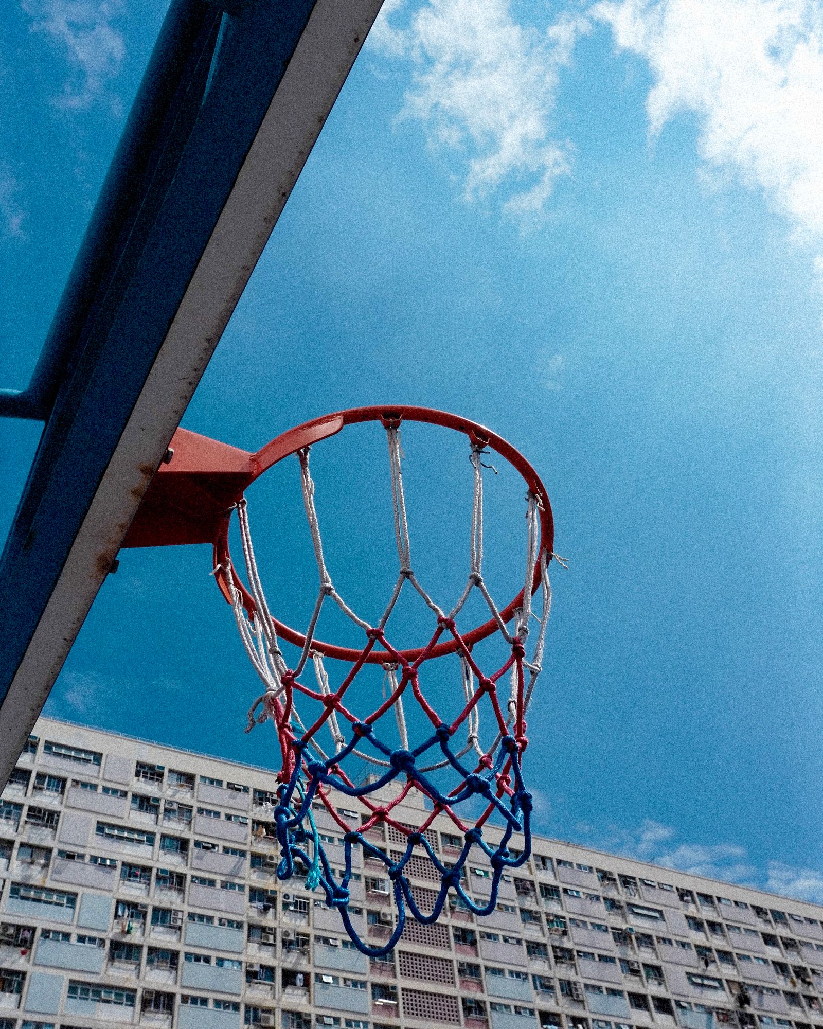 A basketball hoop and backboard rising into a deep blue sky above a housing estate.