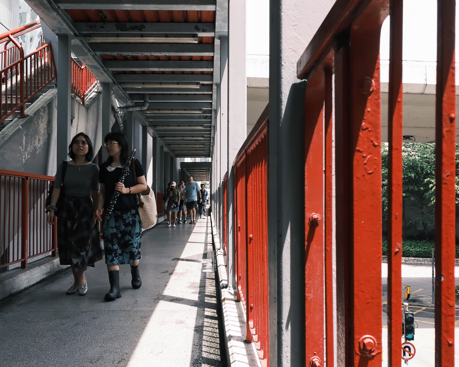 Two people walking through a long red-painted open corridor.