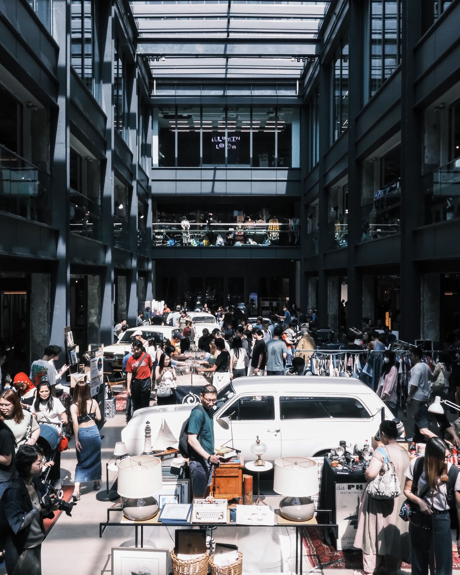 A crowd gathered around white cars in a covered courtyard, seen from above.