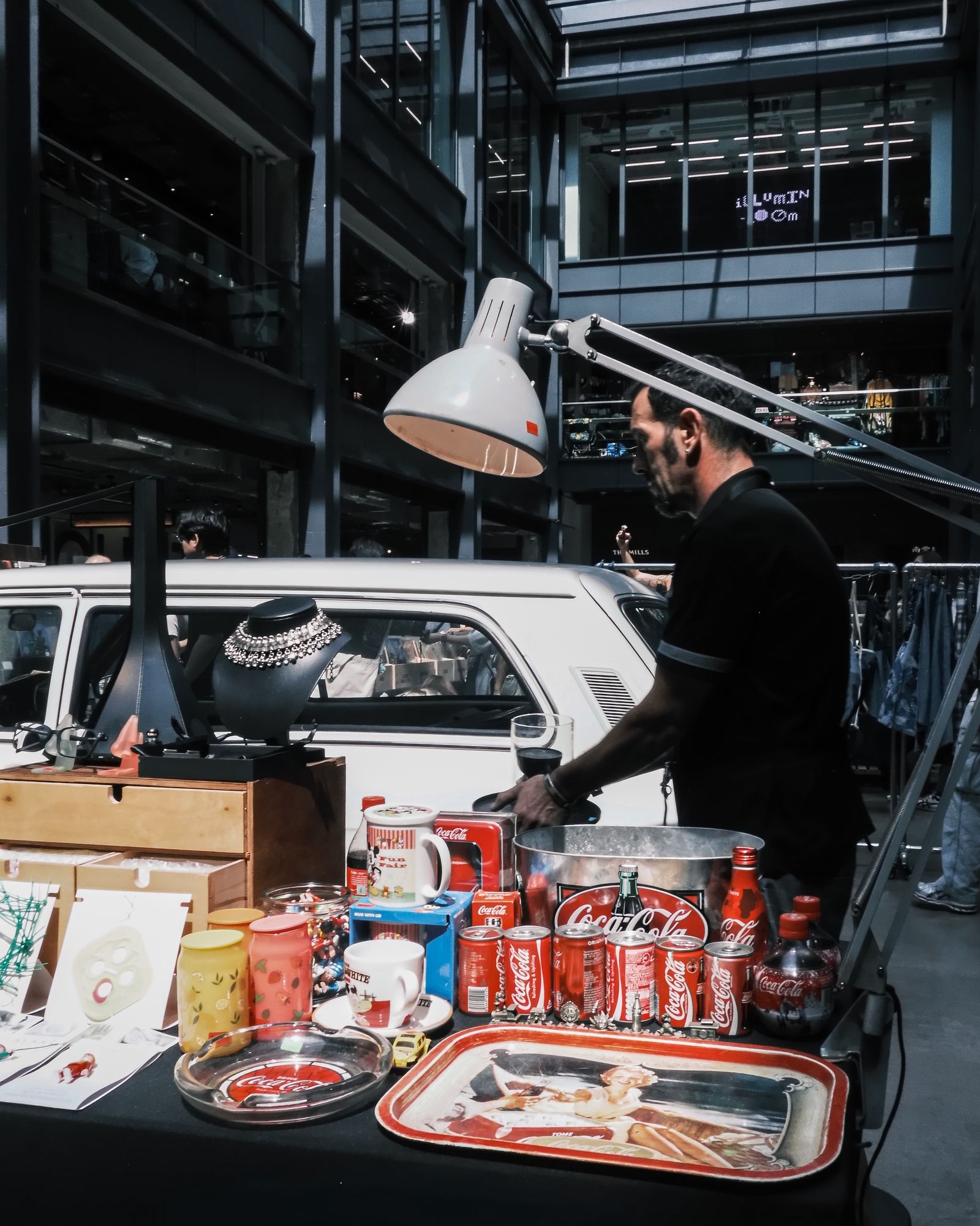 A vendor working under a lamp beside a car at an indoor market.