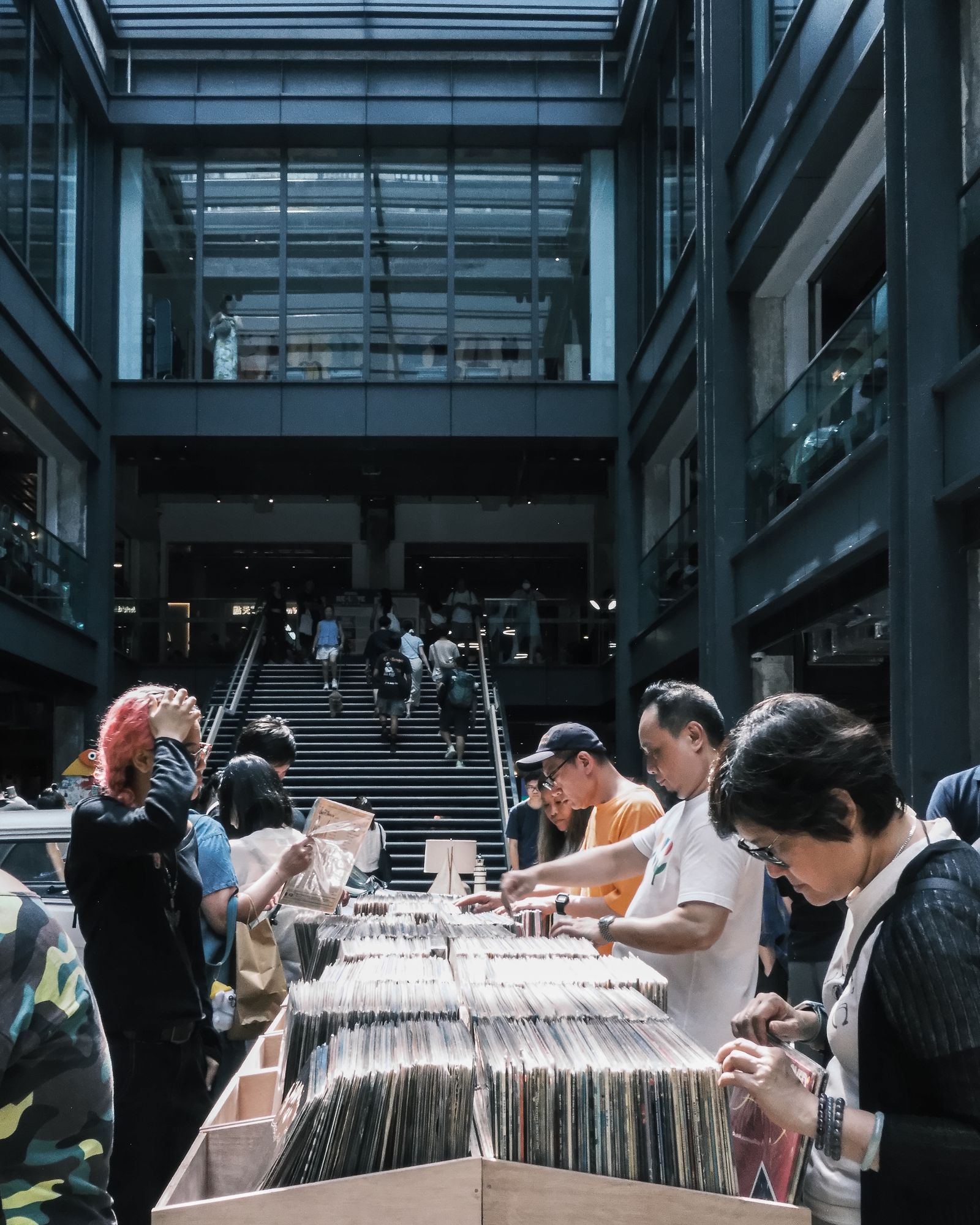 People browsing tables under the concrete canopy of an industrial building.