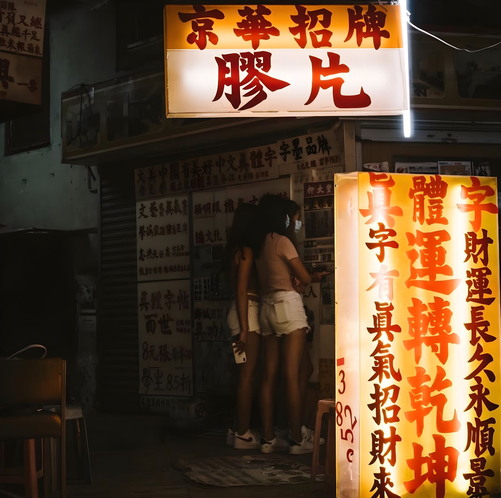 A brightly lit shopfront with layered neon signs on a Hong Kong street at night.