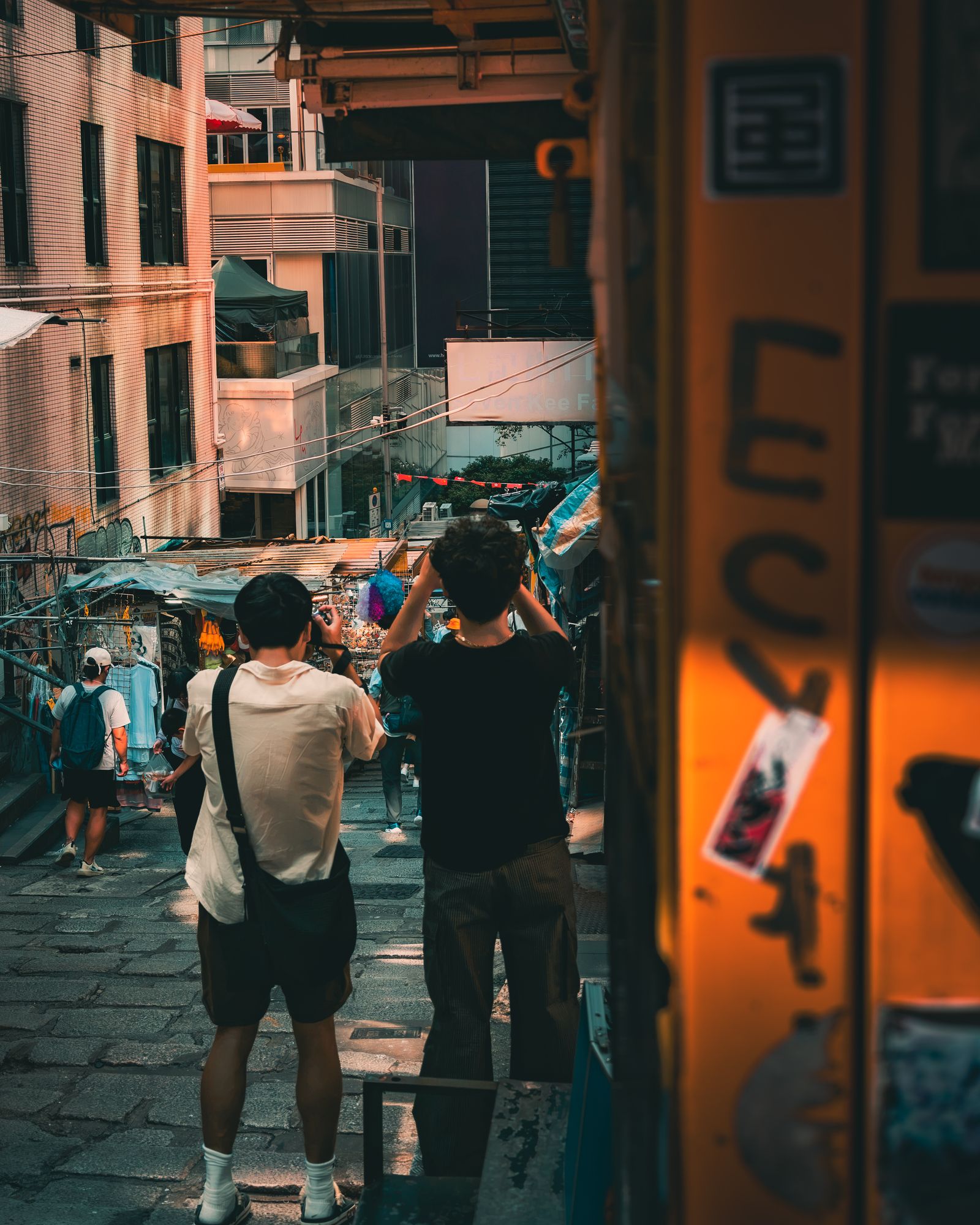 Two photographers working on a crowded Hong Kong street at dusk.