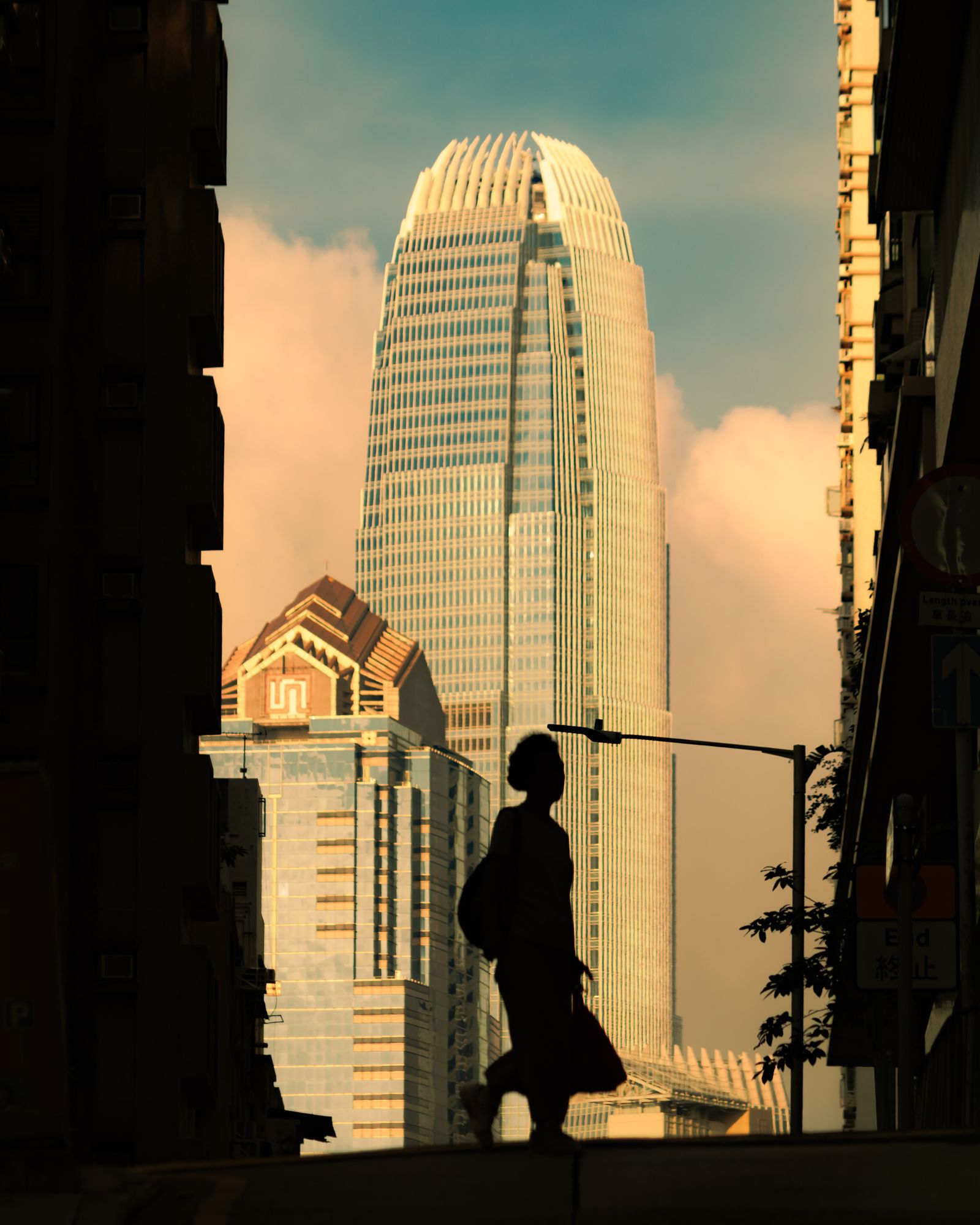 Pedestrians crossing a Hong Kong street at dusk, seen in silhouette.