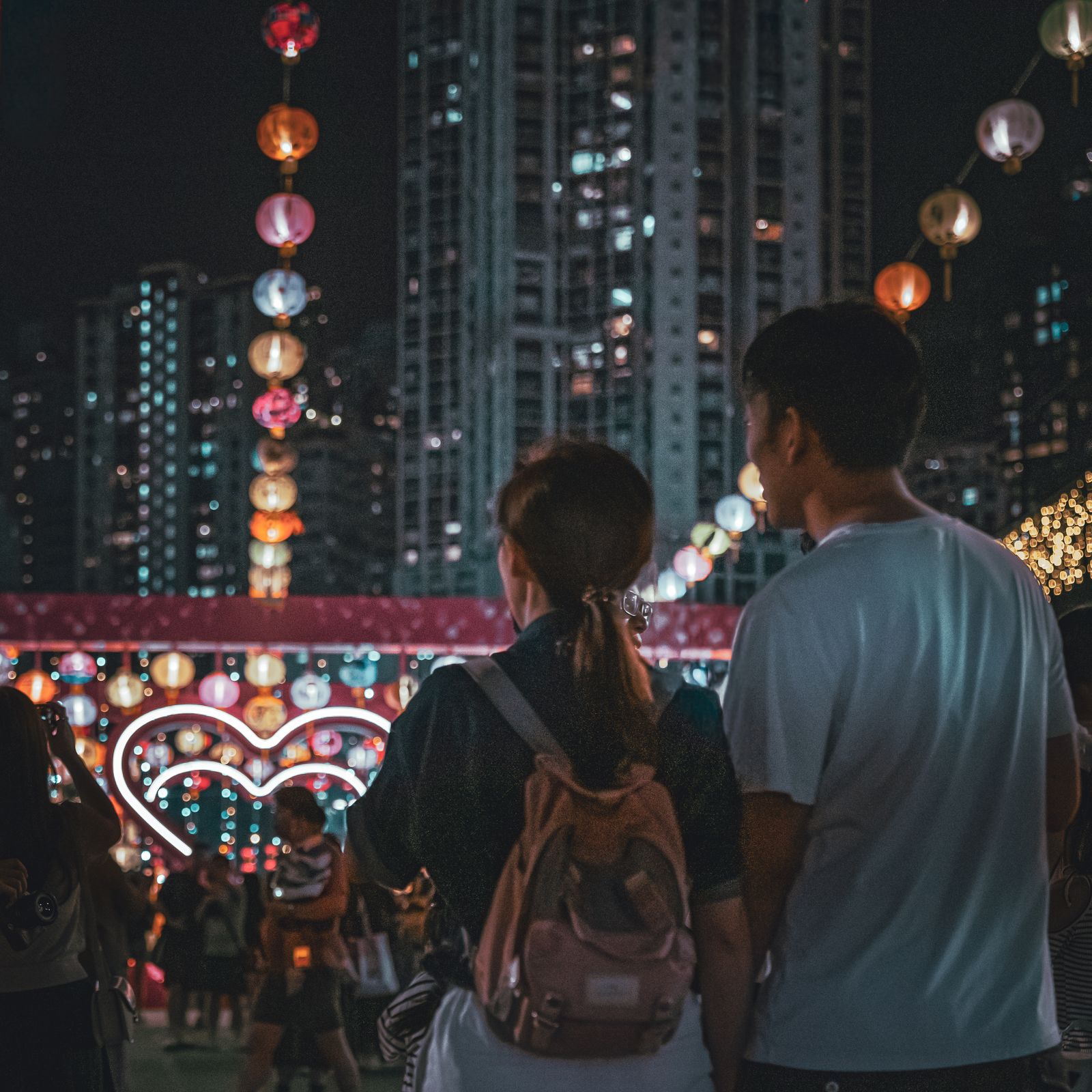 A couple standing beneath lanterns with the city behind them.