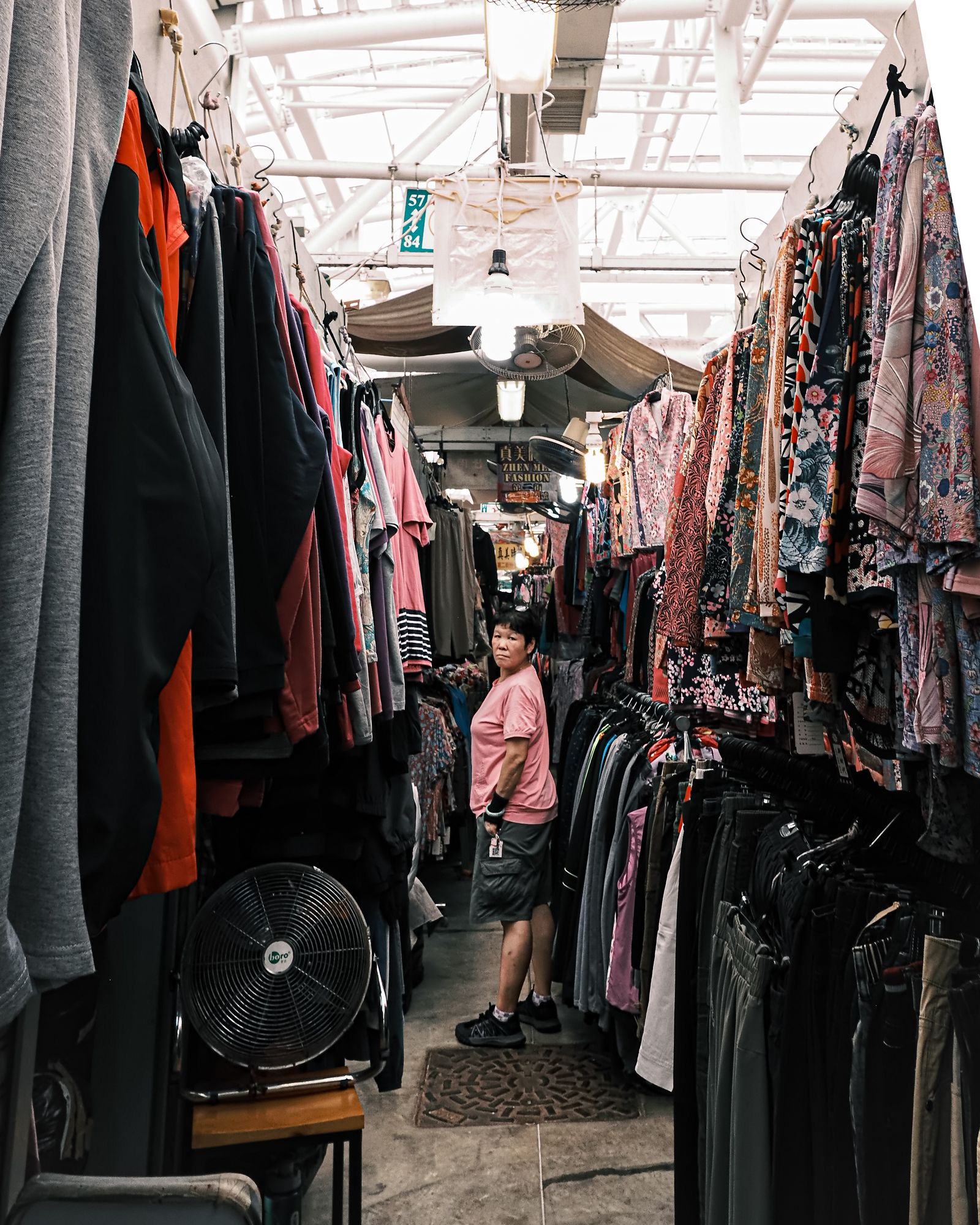 A narrow aisle of hanging clothes and bags inside a Hong Kong market.