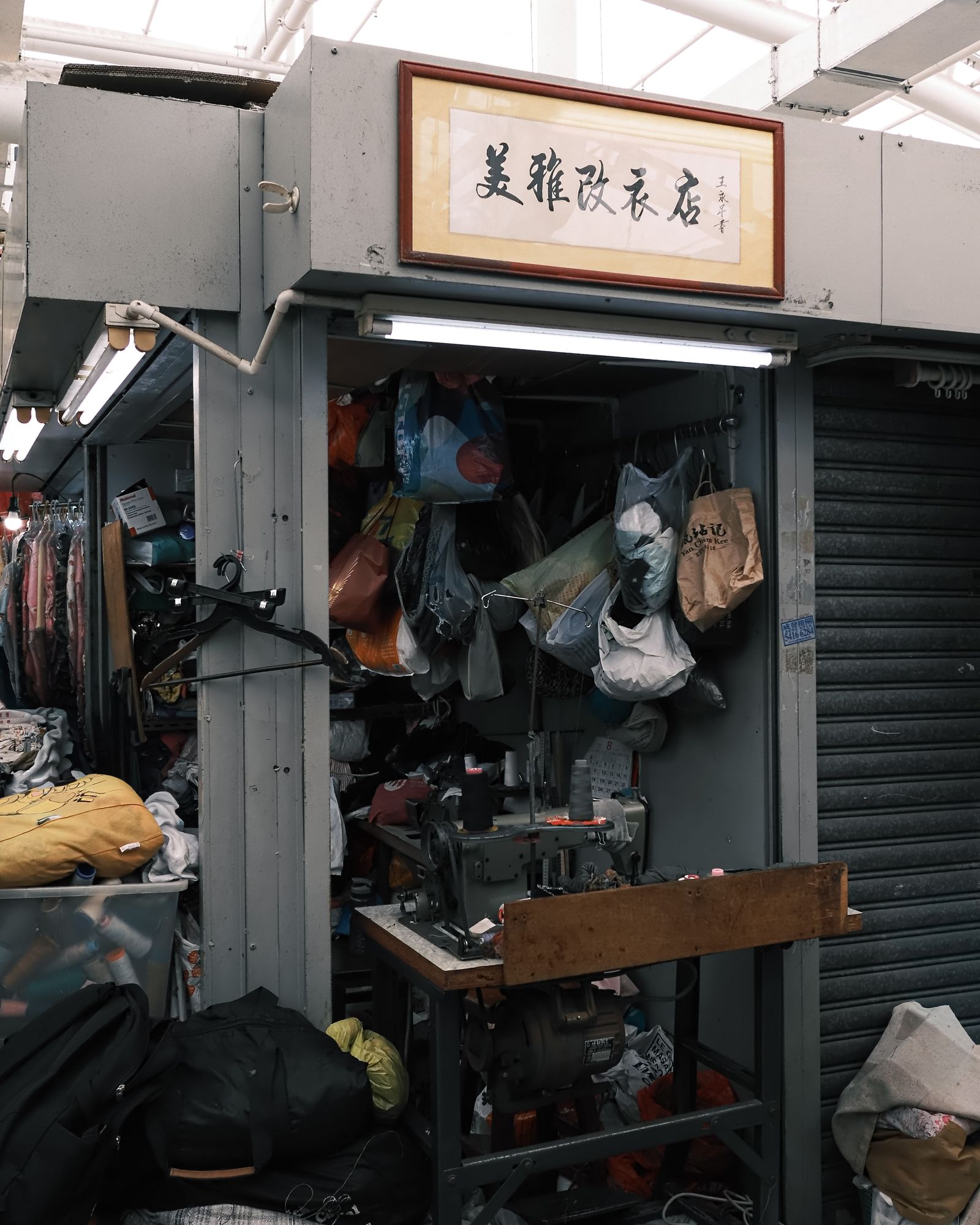 A shopkeeper standing among clothes and objects in a small Hong Kong shop.