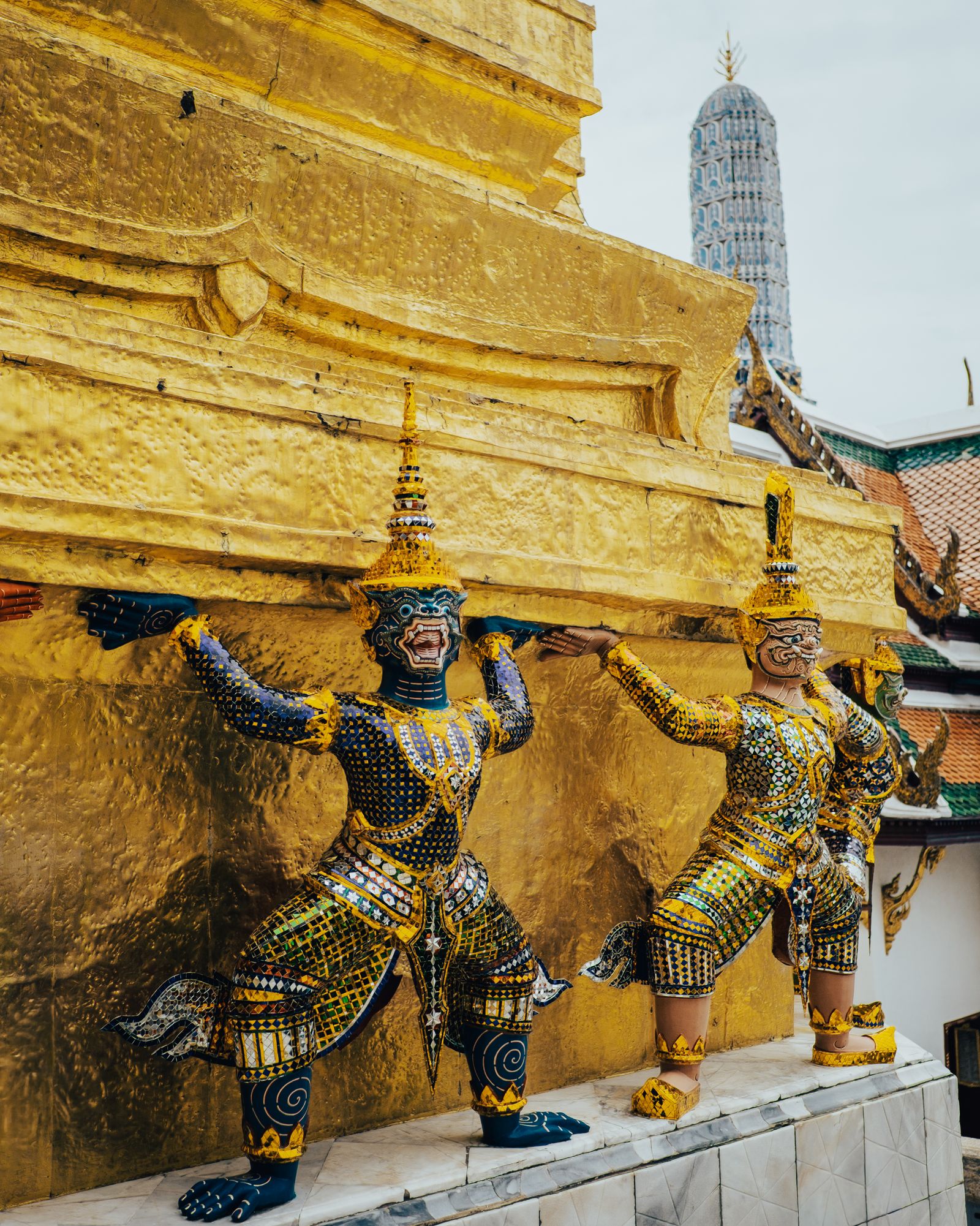 An ornate demon guardian statue in gold and green at a Bangkok temple.