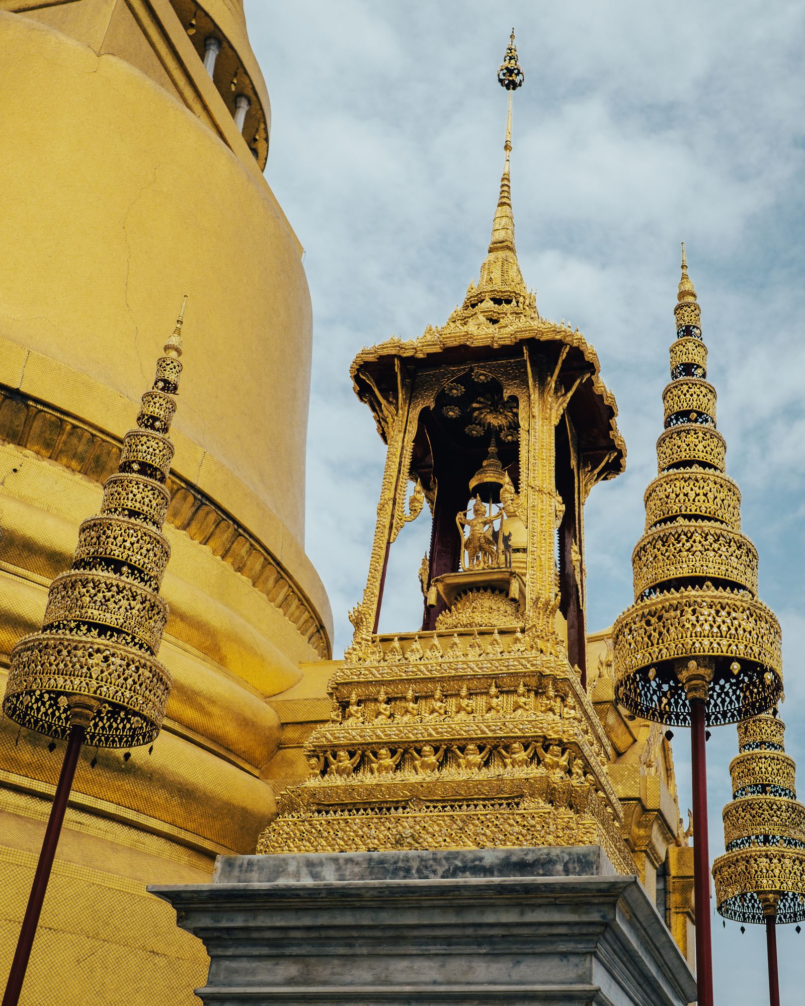 A golden stupa and an ornate golden pavilion rising into a pale sky.