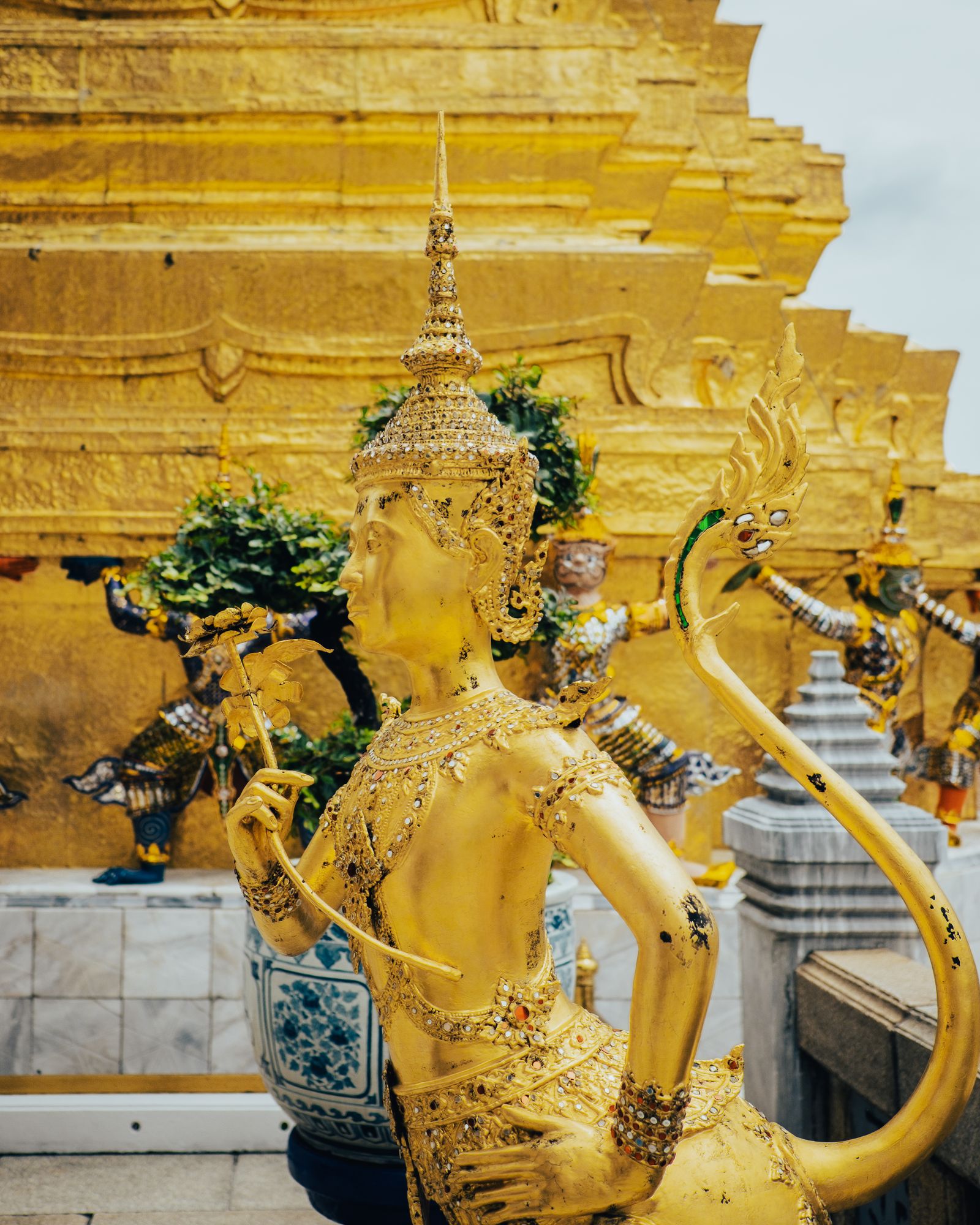 A gilded temple guardian statue surrounded by green foliage.