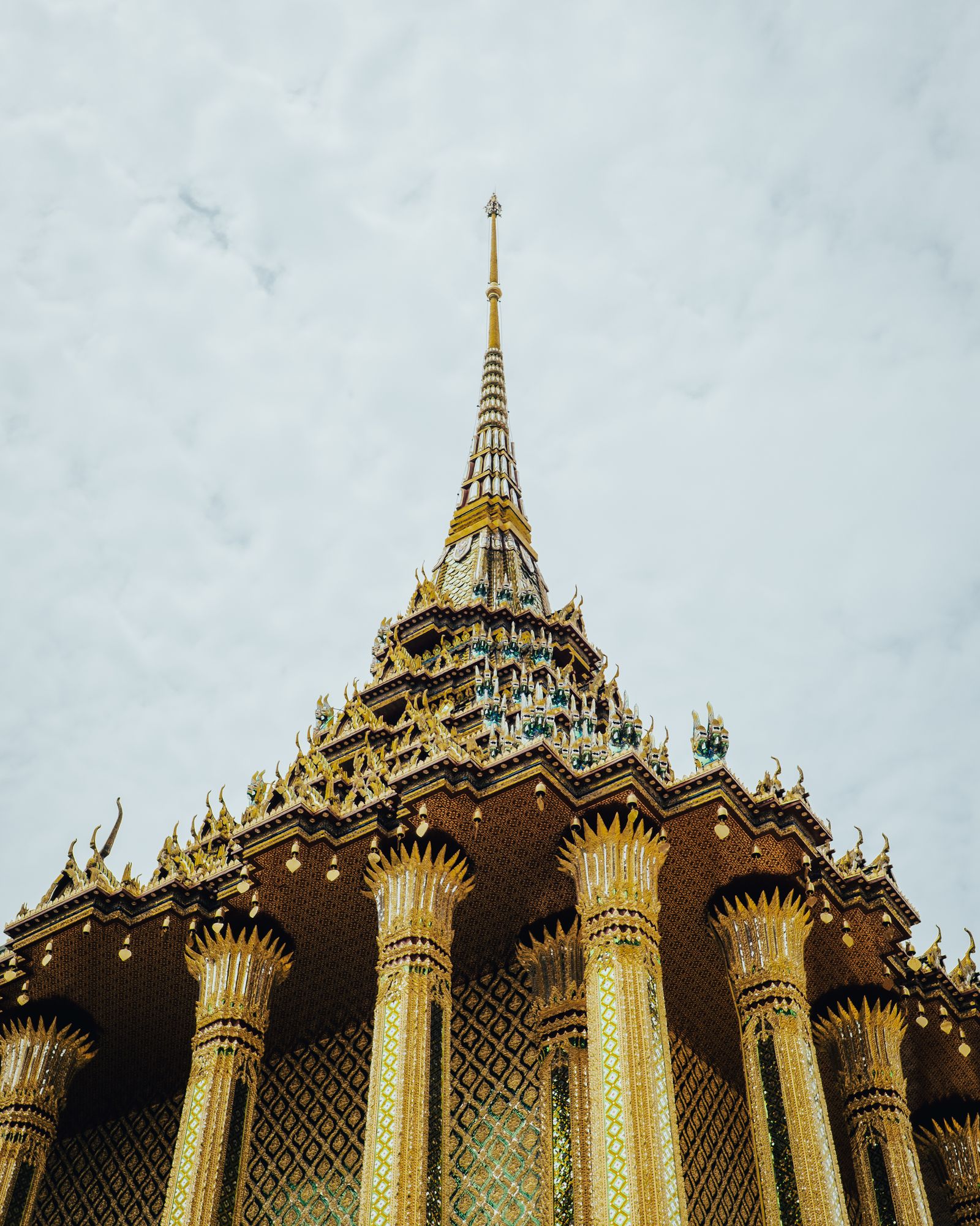 A tall golden stupa with intricate tiers against a pale sky.