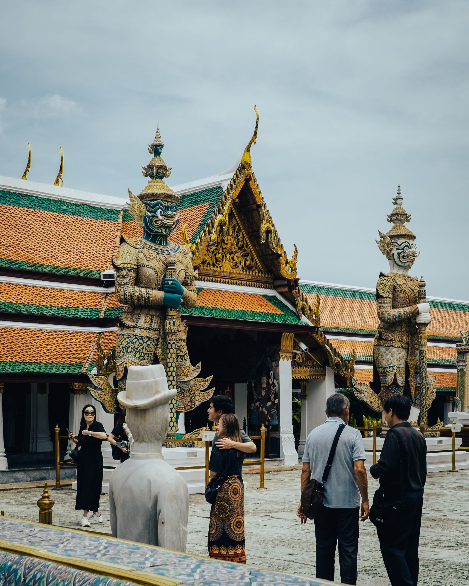 Two ornate guardians flanking a temple courtyard where visitors stand in the sun.