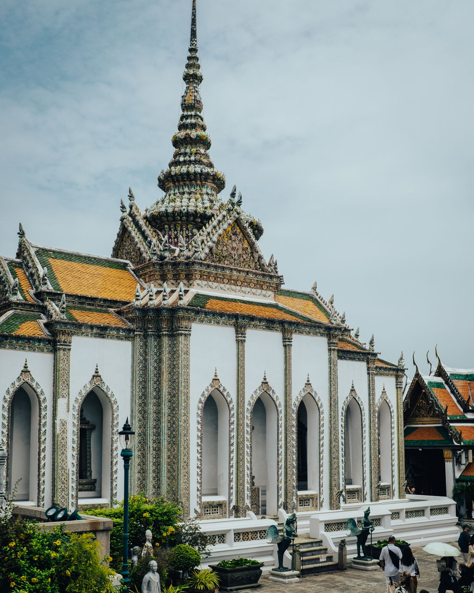 A white temple building with gold details and a tall spire under a pale sky.
