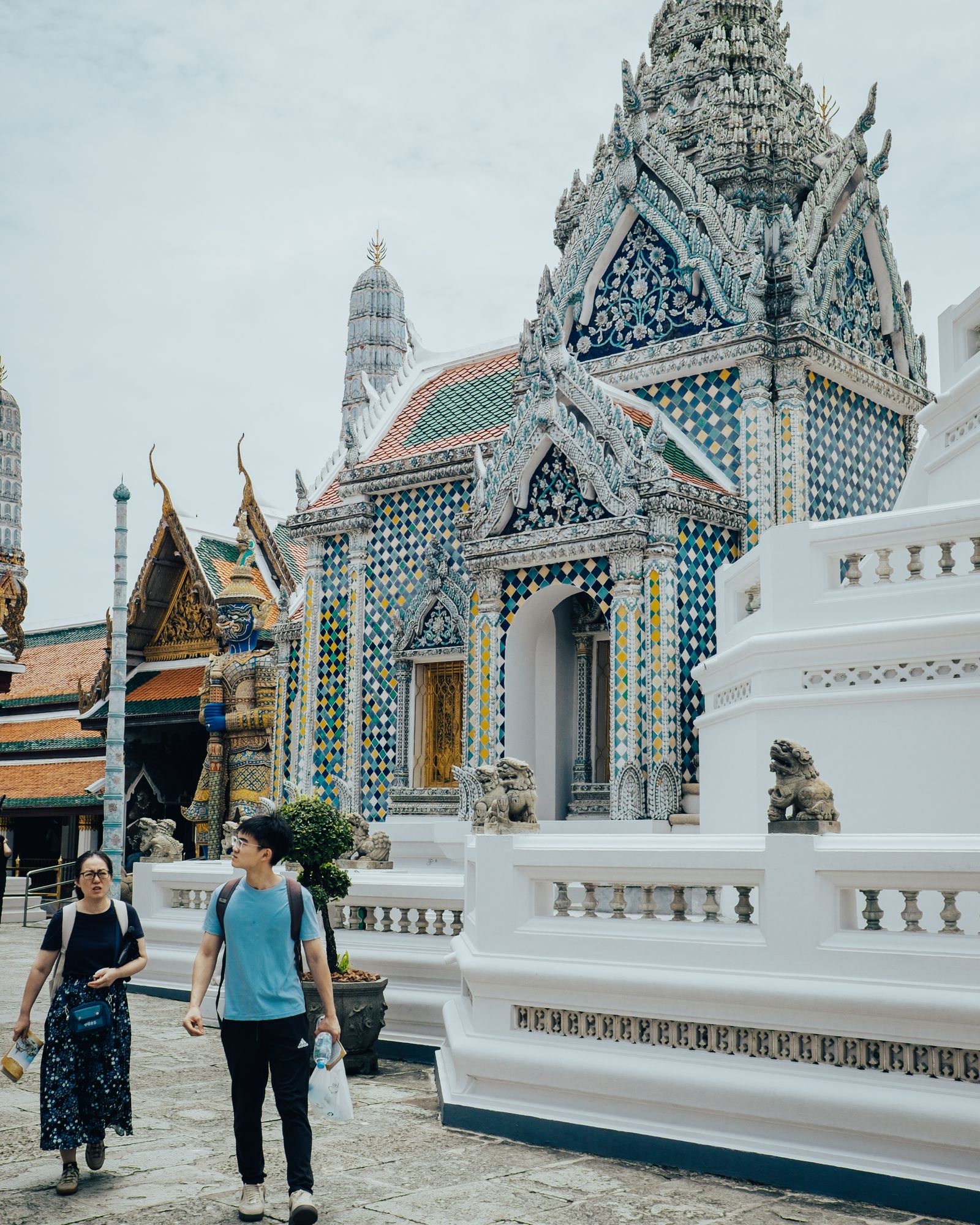 Two visitors walking past an ornate temple building with a patterned roof.