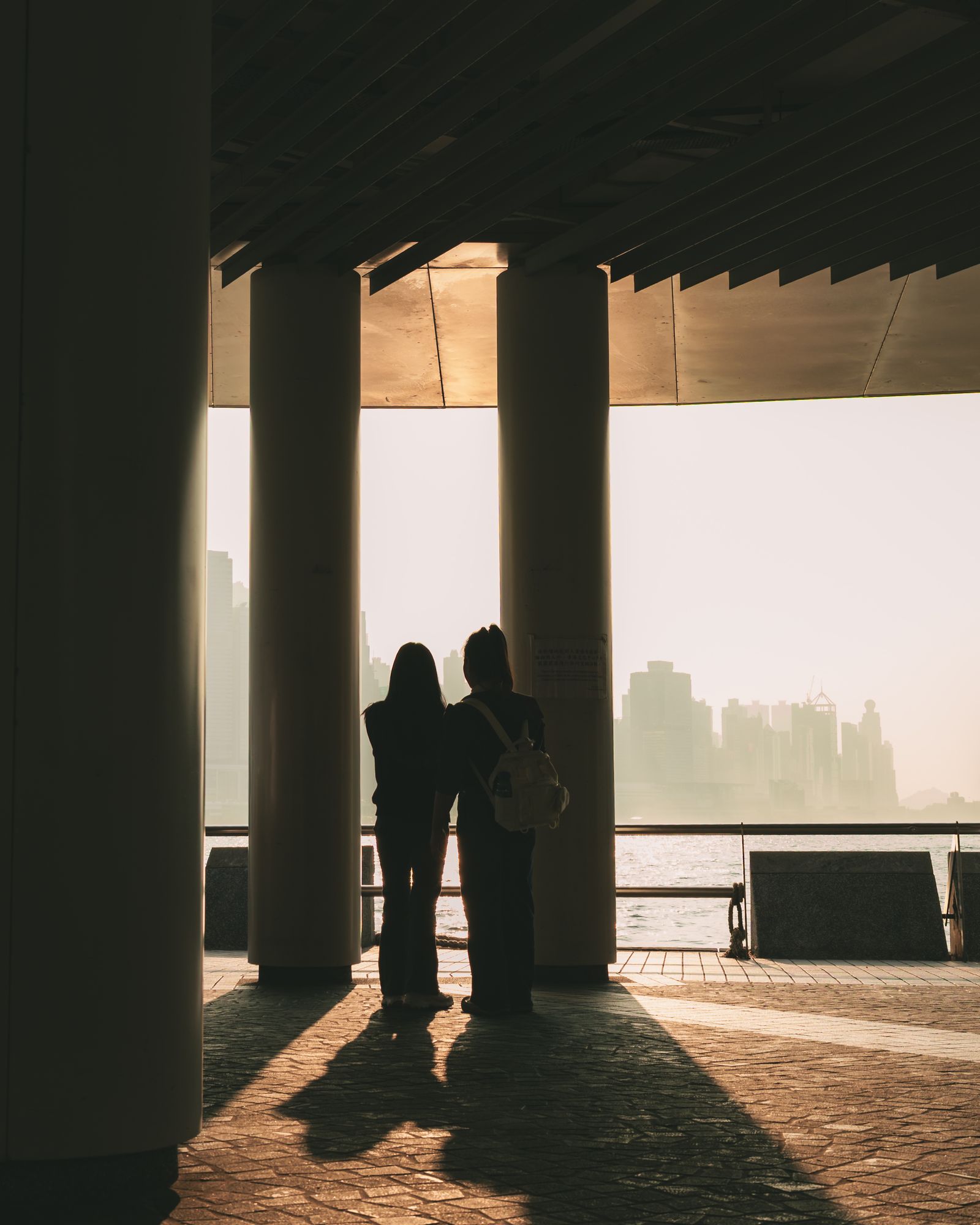 Two figures standing between tall pillars, framed by hard light and long shadows.